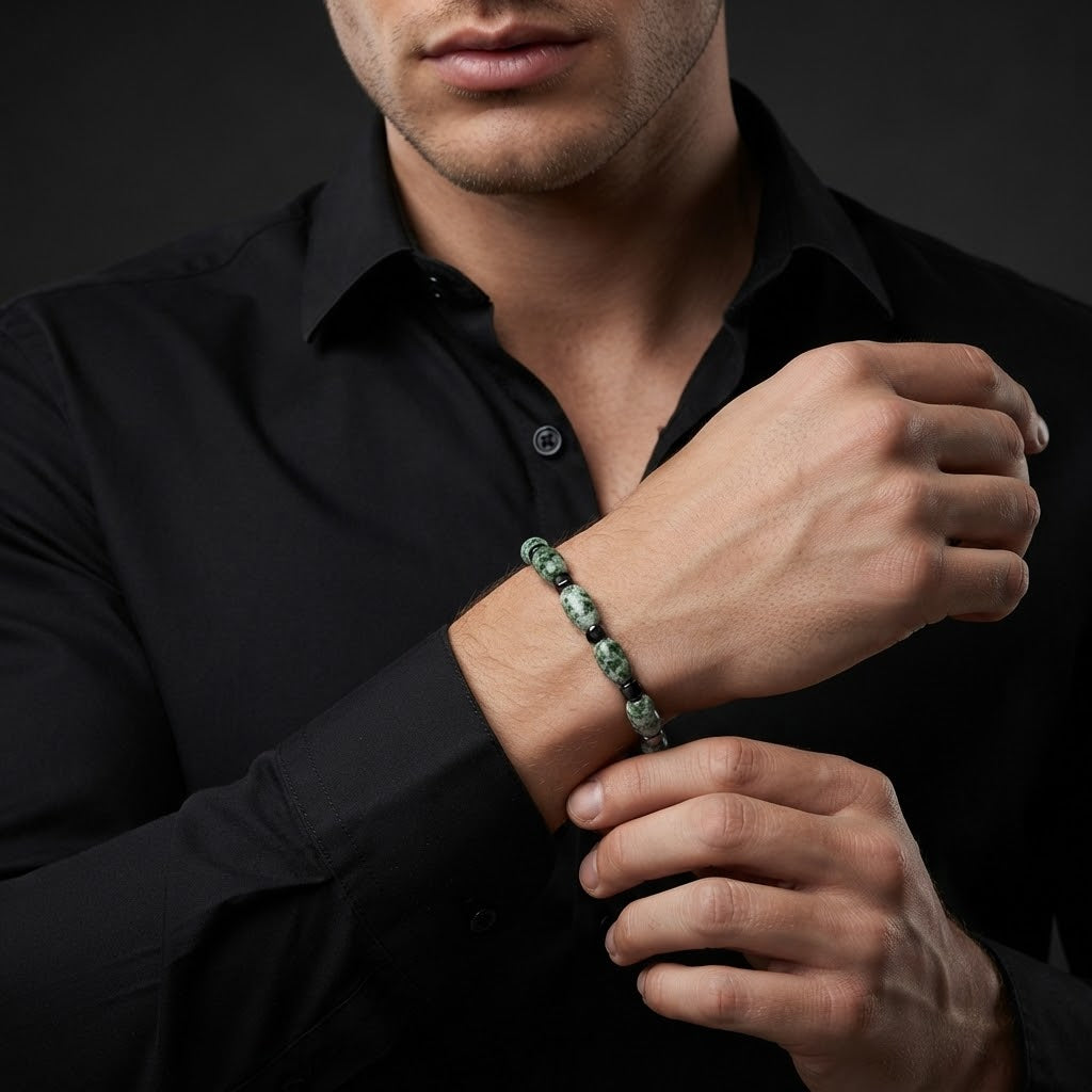 A close-up of a man wearing a green marbled beaded bracelet on his wrist, dressed in a black button-down shirt against a dark studio background.