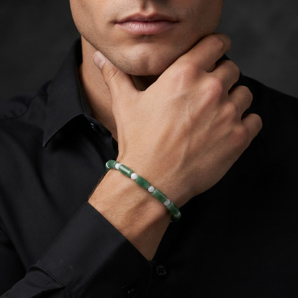 A close-up of a man wearing a green beaded bracelet with white inlaid accents, styled with a black collared shirt against a dark background.