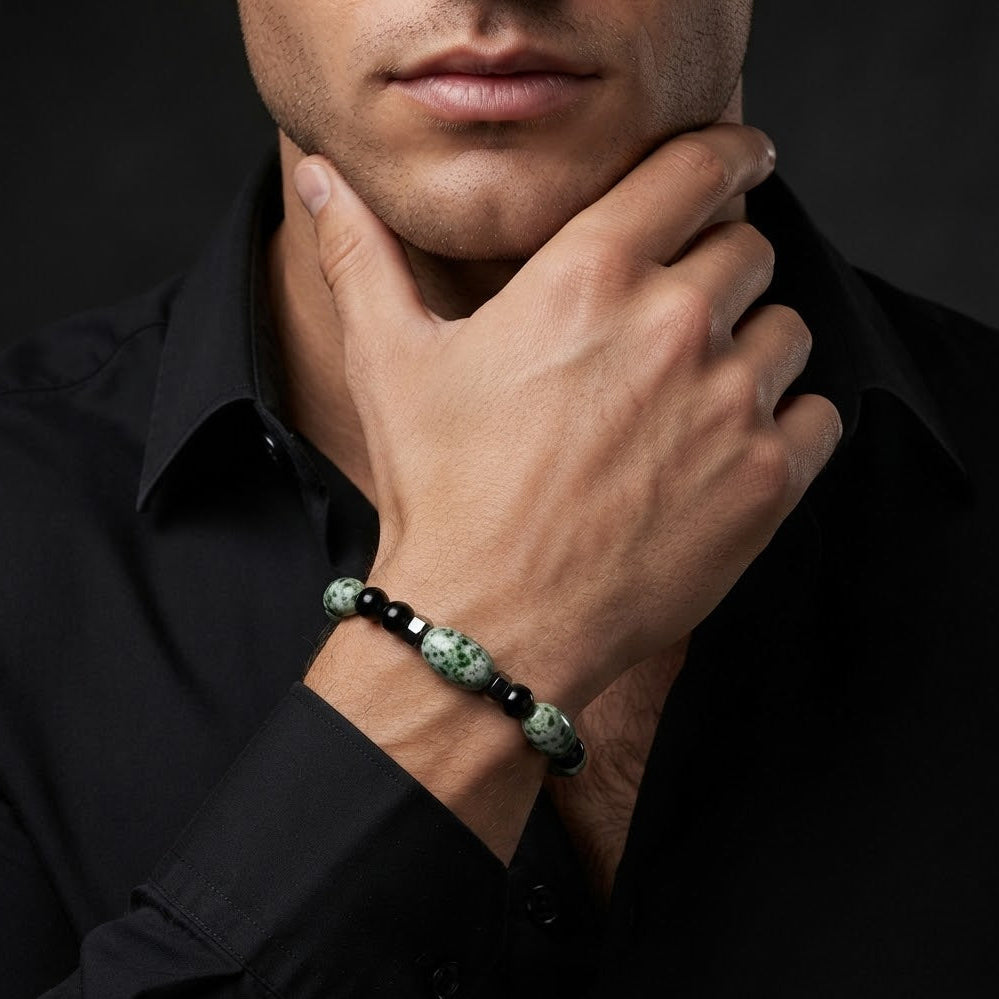A close-up of a man wearing a beaded bracelet on his wrist, dressed in a black shirt against a dark background.