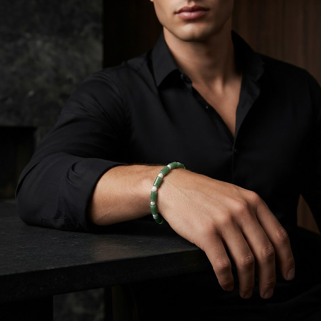 A man wearing a black button-down shirt rests his arm on a dark table, showcasing a green beaded bracelet on his wrist.