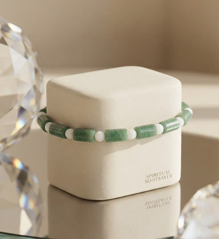 A beaded bracelet with green and white cylindrical beads displayed on a cream-colored jewelry box. The box has the text 'SPIRITUAL SOULSAYER' printed on the front.