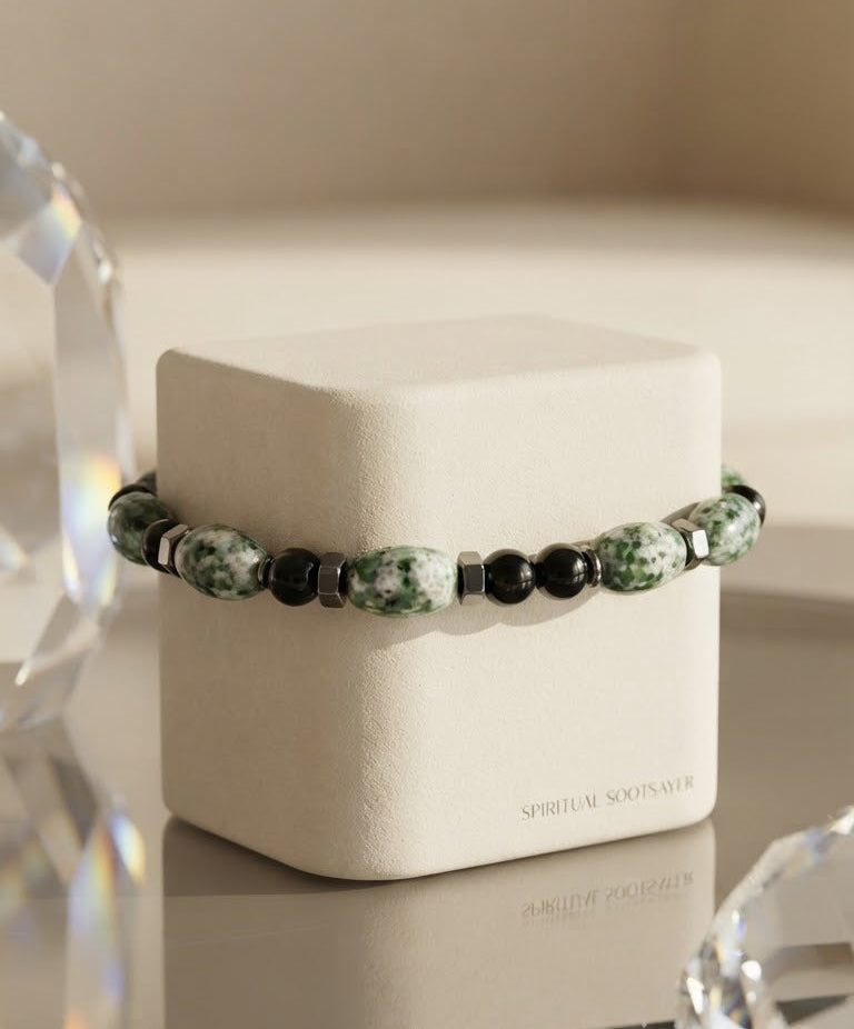 A beaded bracelet with green and white marbled beads and black beads, displayed on a cream-colored jewelry box. The box has the brand name 'SPIRITUAL SOULS A.