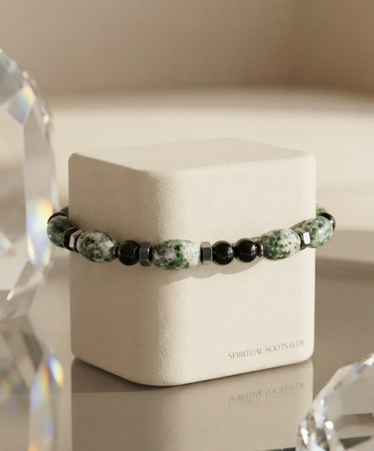 A beaded bracelet with green and white marbled beads and black beads, displayed on a cream-colored jewelry box. The box has the brand name 'SPIRITUAL SOULS A.
