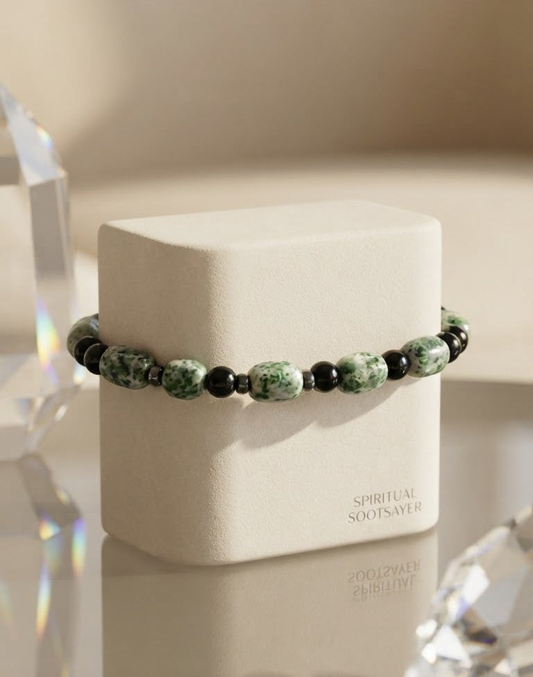 A beaded bracelet with green and white marbled beads separated by small black beads, displayed on a cream-colored jewelry box. The box has the text 'SPIRITUAL SOOTSAVER' printed on it.