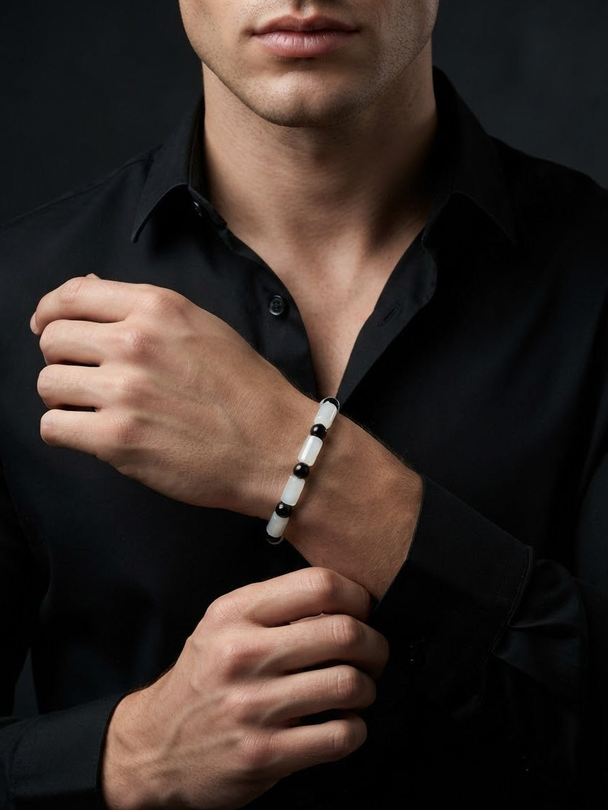 A close-up of a man wearing a black button-down shirt and adjusting his cuff while wearing a white beaded bracelet with small black beads on his wrist.