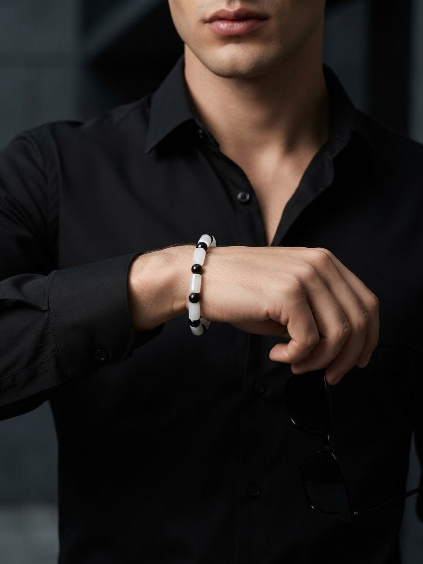 A close-up of a man wearing a black button-down shirt and a white beaded bracelet with black beads, adjusting the bracelet on his wrist.