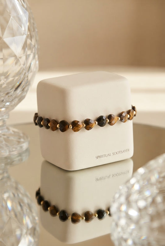 A beaded bracelet with brown and black tiger's eye beads and small gold spacer beads, displayed on a white cube box labeled 'SPIRITUAL SOCKSFAVER'.
