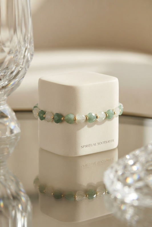 A beaded bracelet with light green and white beads separated by small gold spacer beads, displayed on a white cube-shaped box. The box has the brand name 'SPIRITUAL SOULS' printed on the front.