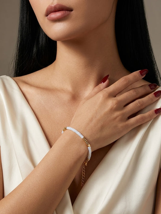 A close-up of a woman wearing a delicate white beaded bracelet with gold-toned chain details on her wrist, paired with a cream satin dress.