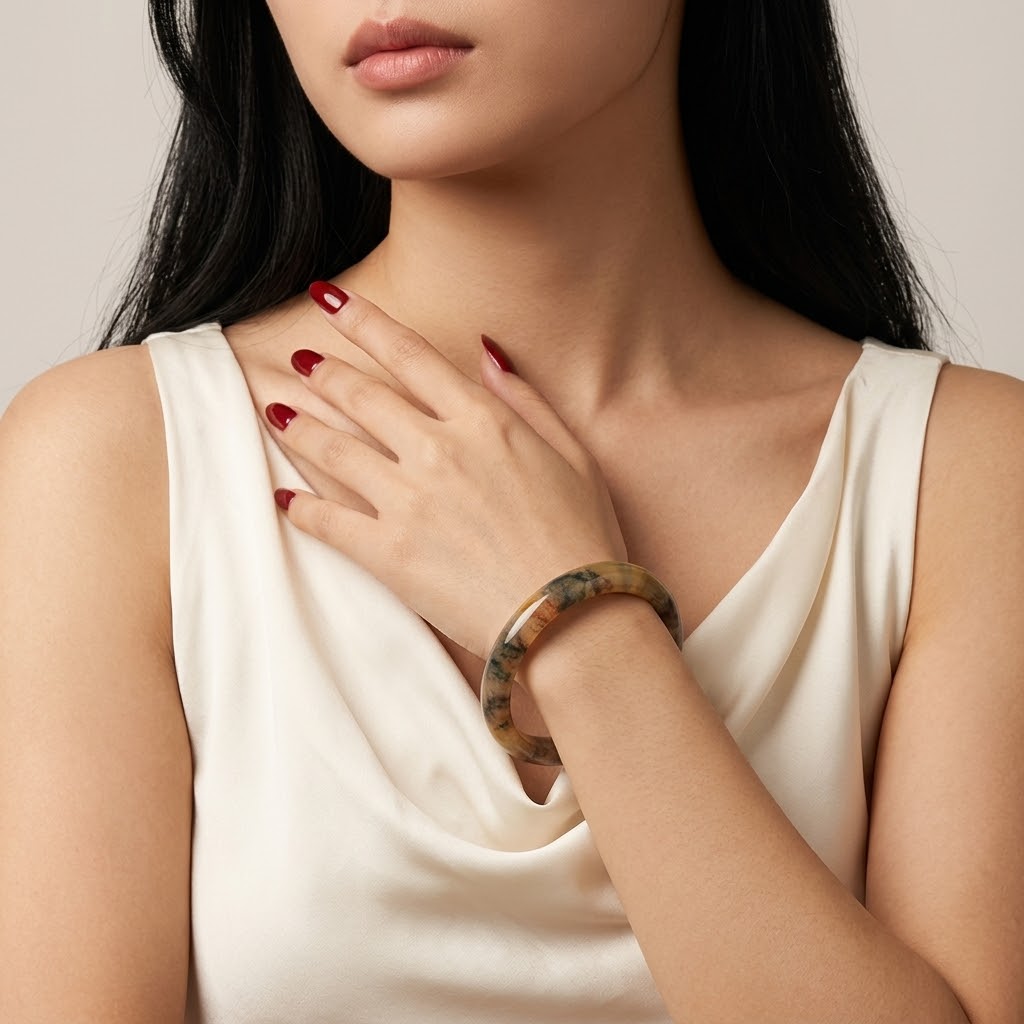 A close-up of a woman wearing a thick, polished tortoiseshell bangle bracelet on her wrist, paired with a cream-colored satin top. The background is a solid, warm off-white studio backdrop.