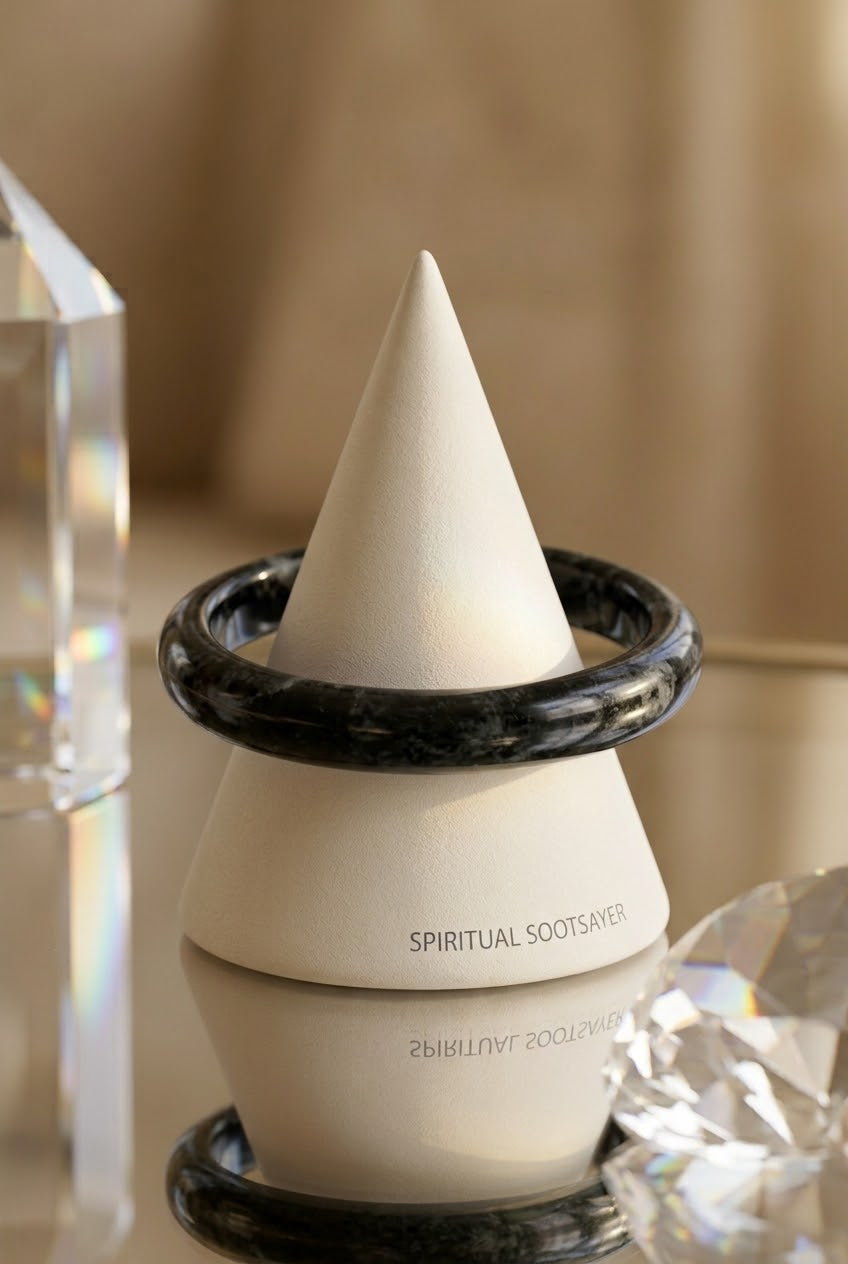 A white cone-shaped product labeled 'SPIRITUAL SOOTSAVER' displayed on a matching white and black marbled base, with crystal props and a soft beige background.