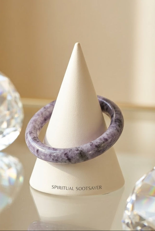 A lavender and purple marbled spiritual sootseyer bracelet displayed on a white cone stand, surrounded by decorative clear crystal spheres on a reflective surface.