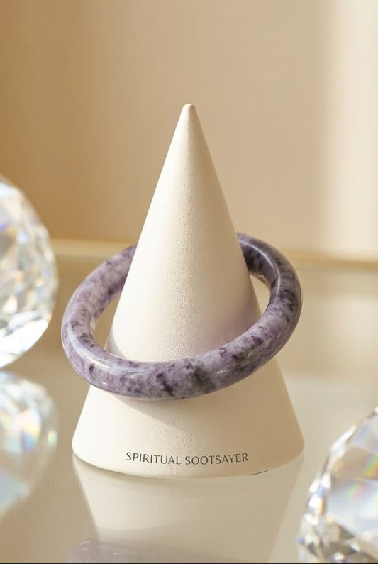 A lavender and purple marbled spiritual sootseyer bracelet displayed on a white cone stand, surrounded by decorative clear crystal spheres on a reflective surface.