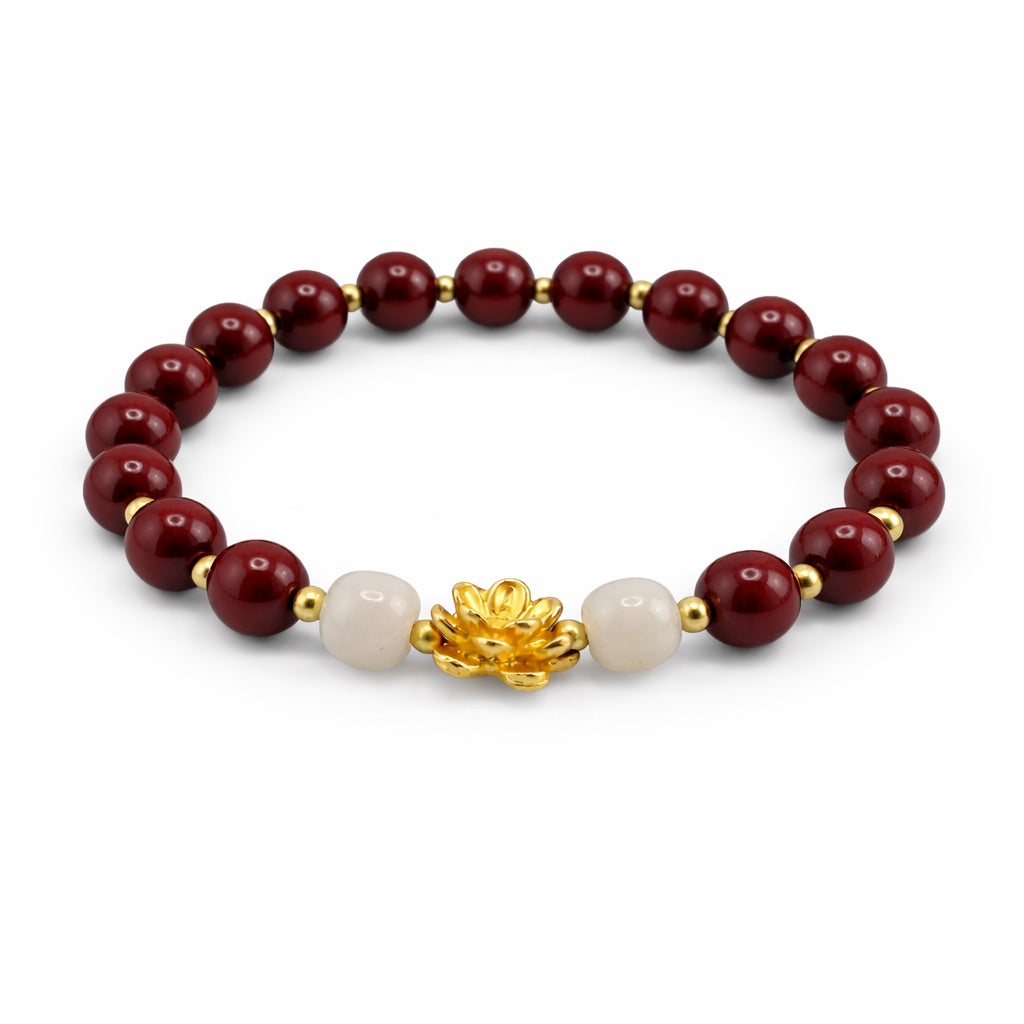Bracelet with red beads, white pearl, and gold lotus charm on a white background