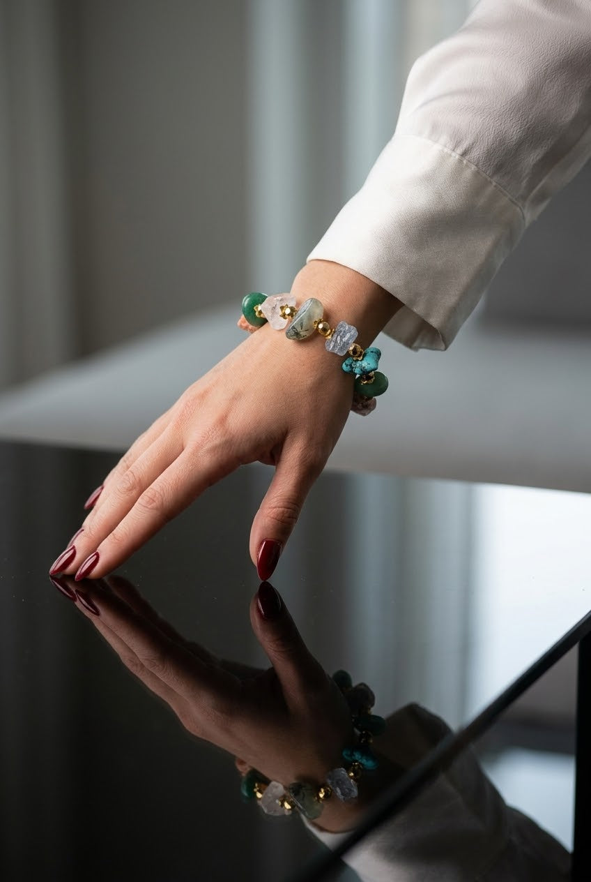 A close-up of a person's hand wearing a beaded bracelet with green, blue, and white beads, resting on a reflective black surface.