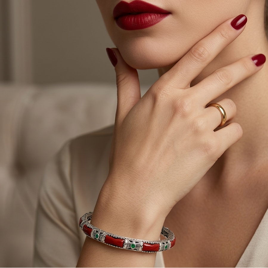Close-up of a woman's hand wearing a red bracelet and gold ring, with a blurred background.