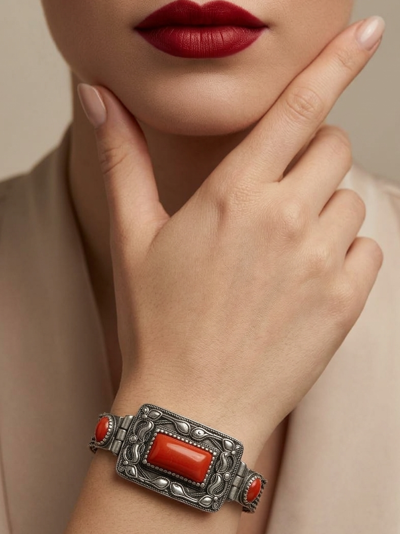 Close-up of a hand wearing a silver bracelet with red stones, against a neutral background.