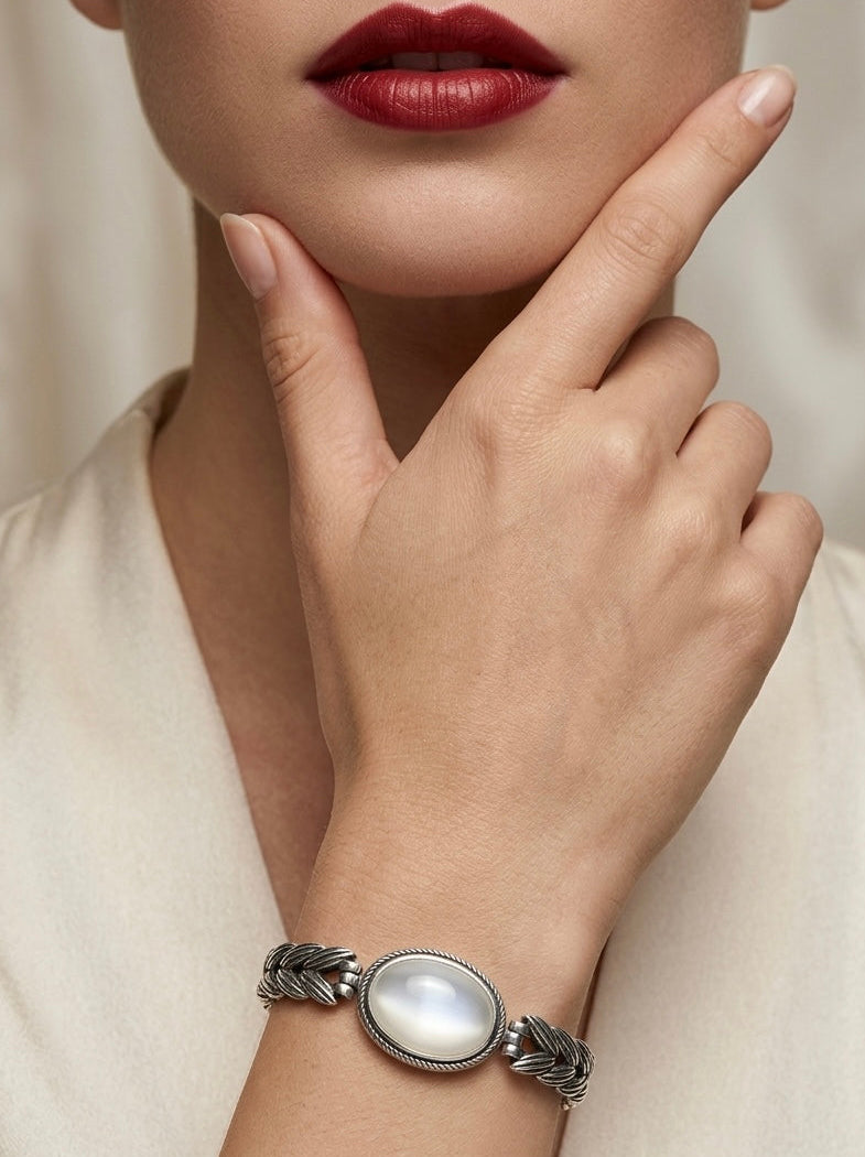Close-up of a woman's hand wearing a silver bracelet with a large stone, against a neutral background.