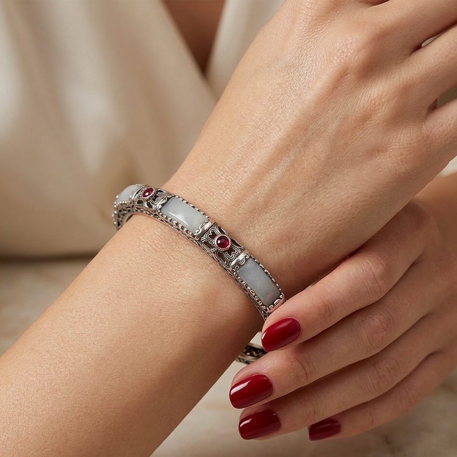 Close-up of a hand wearing a silver bracelet with gemstones on a neutral background