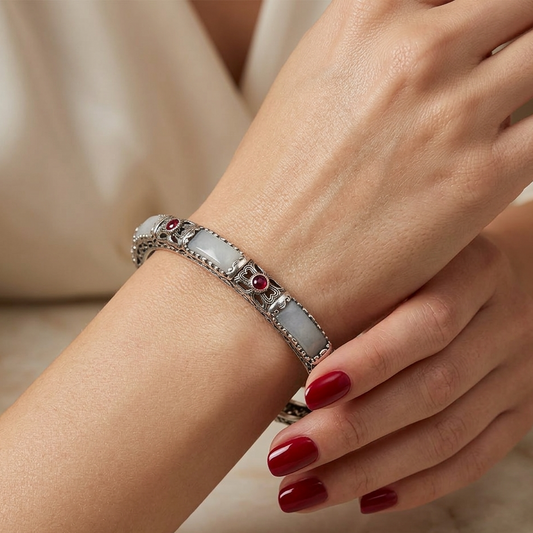 Close-up of a hand wearing a silver bracelet with gemstones on a neutral background