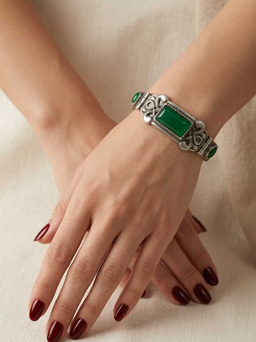 Silver bracelet with green stones on a hand against a beige background