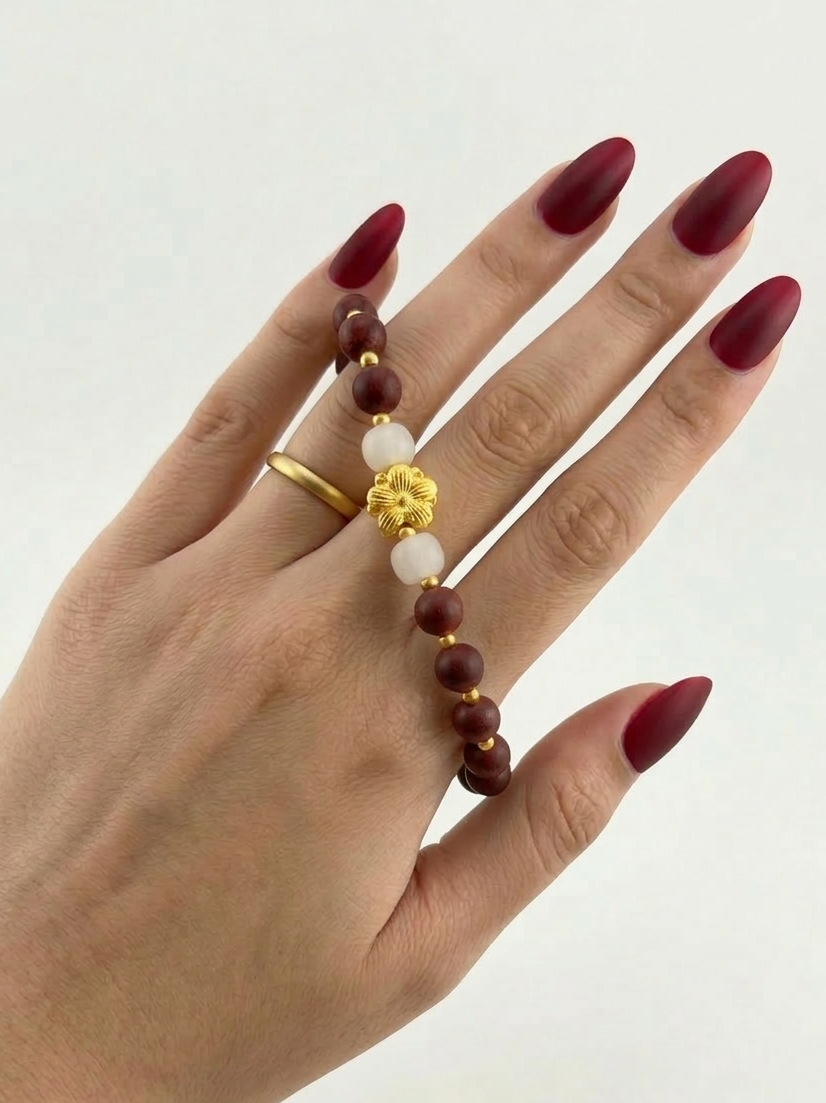 Hand wearing a bracelet and ring with red nail polish on a white background