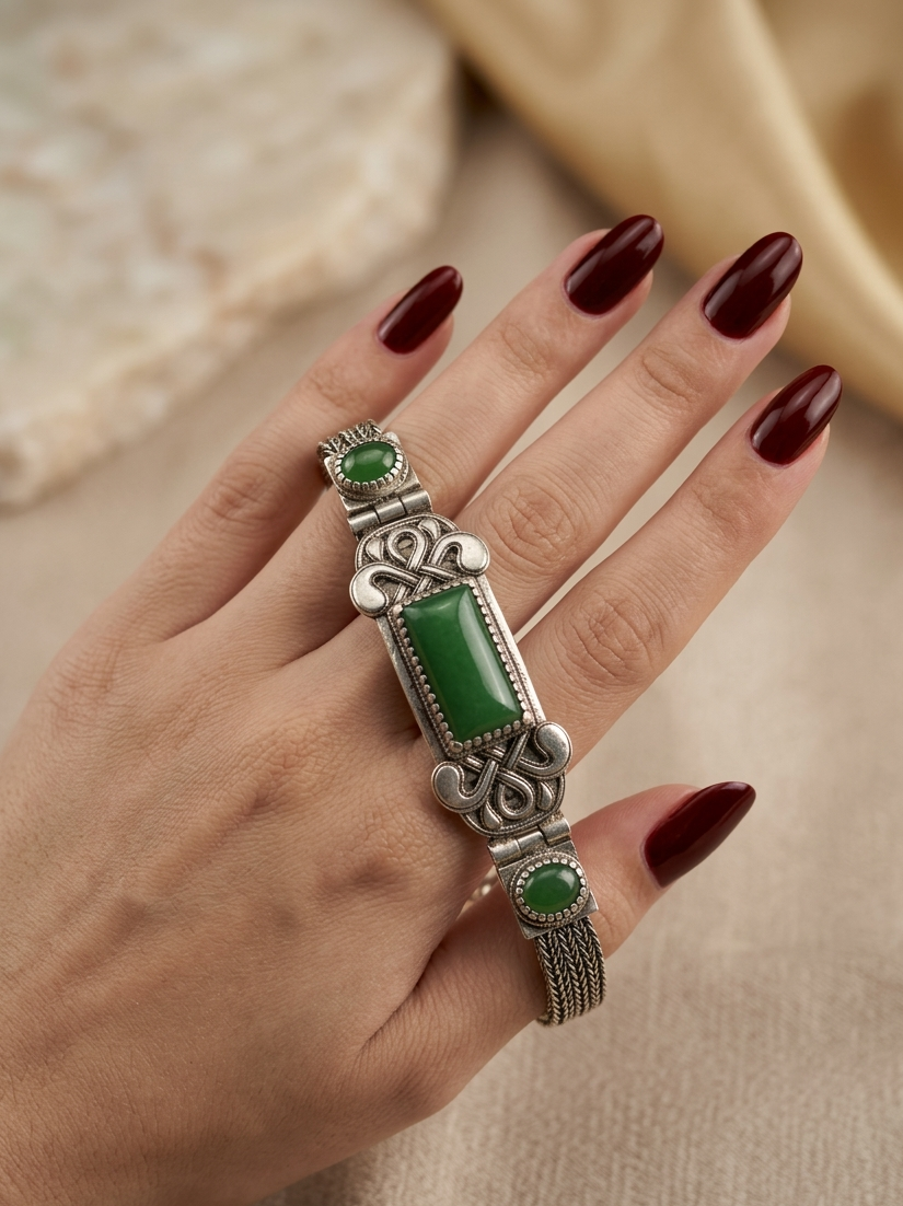 Hand wearing a silver ring with green stones on a neutral background