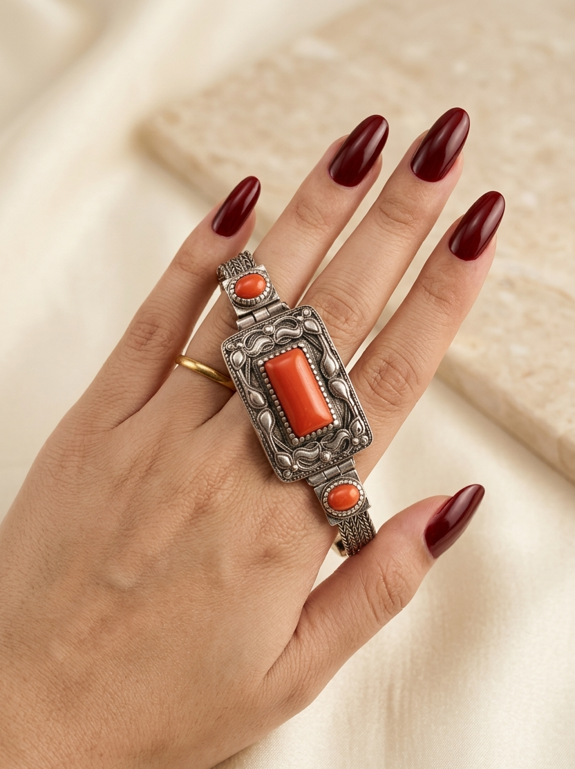 Hand wearing a decorative ring with red stones on a neutral background