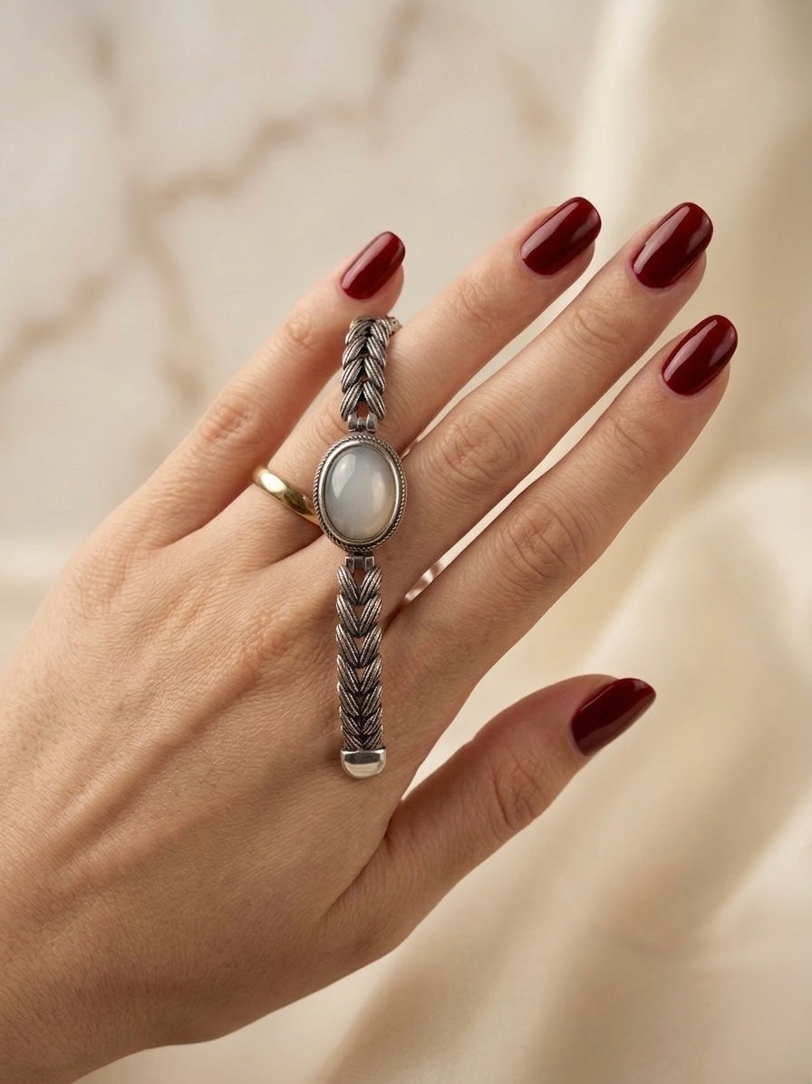 Hand wearing a silver ring with a stone on a neutral background