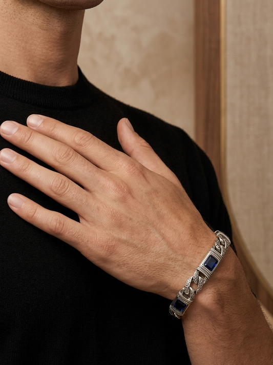 Hand wearing a silver bracelet with blue stones against a neutral background