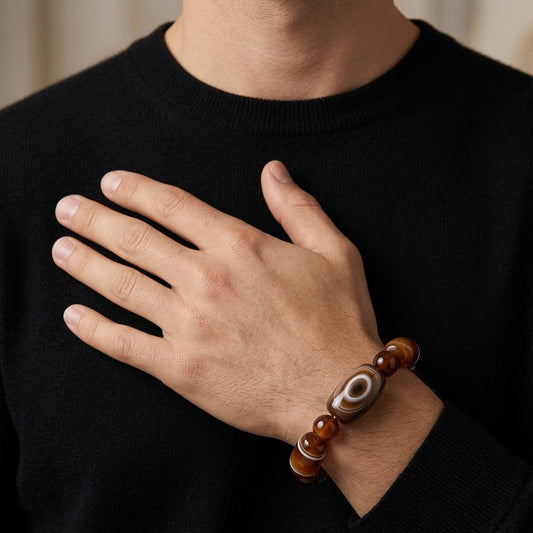 Person wearing a dark sweater with a hand resting on chest, wearing a brown beaded bracelet.