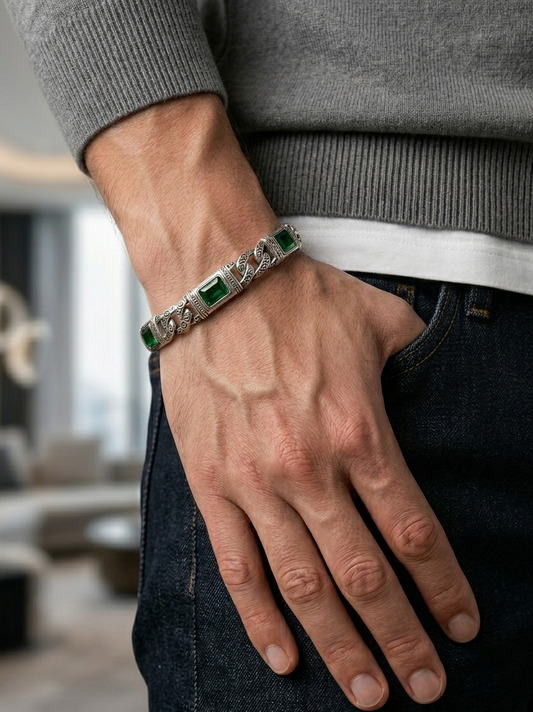 Hand wearing a silver bracelet with green stones, blurred indoor background