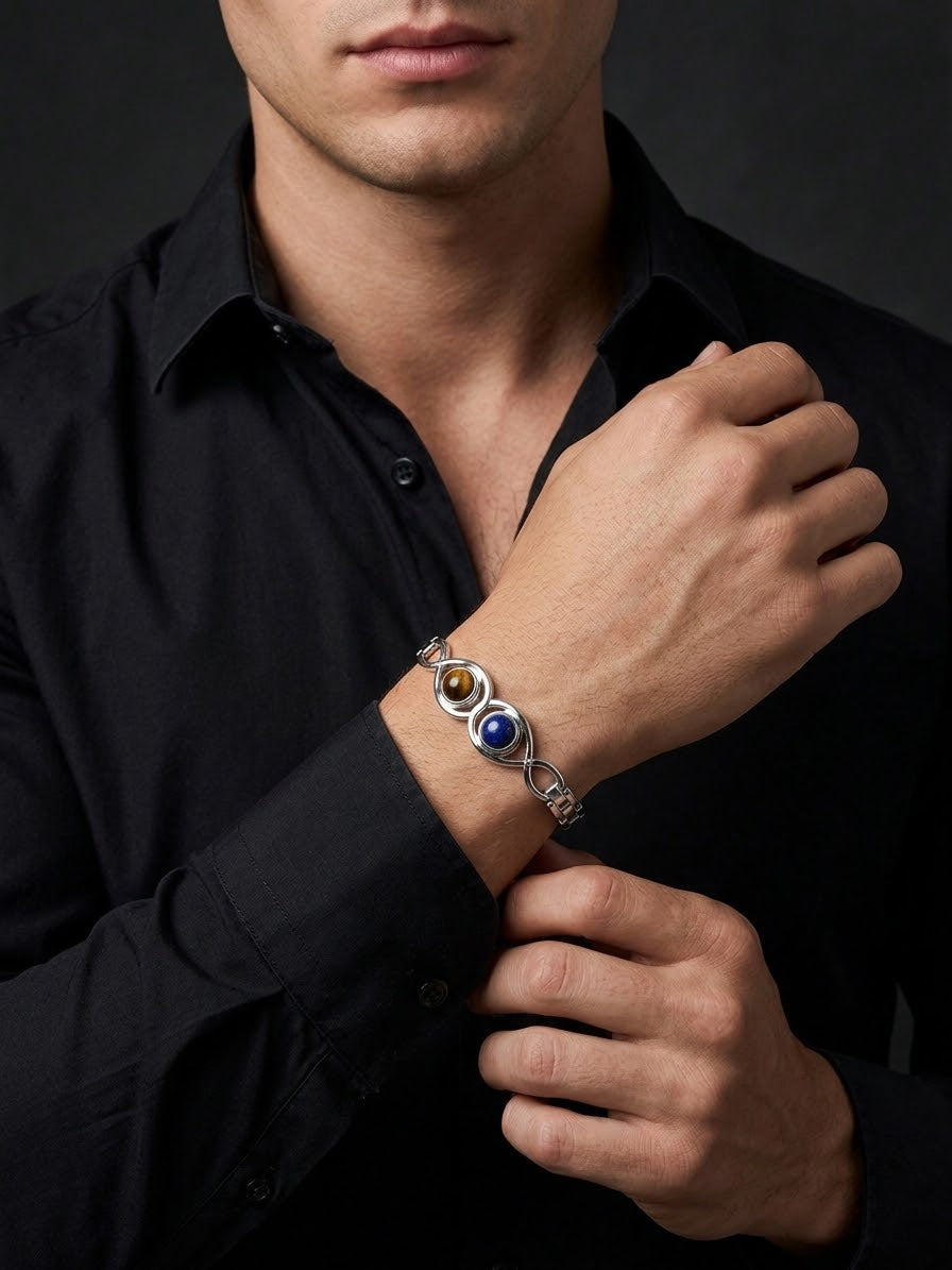 A close-up of a man wearing a silver-toned bracelet with three circular stone accents in brown, blue, and white, paired with a black button-down shirt.