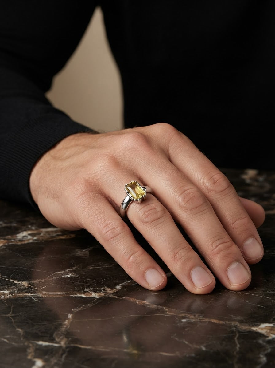 A close-up of a person's hand resting on a dark marble surface, wearing a silver-toned ring with a yellow gemstone.