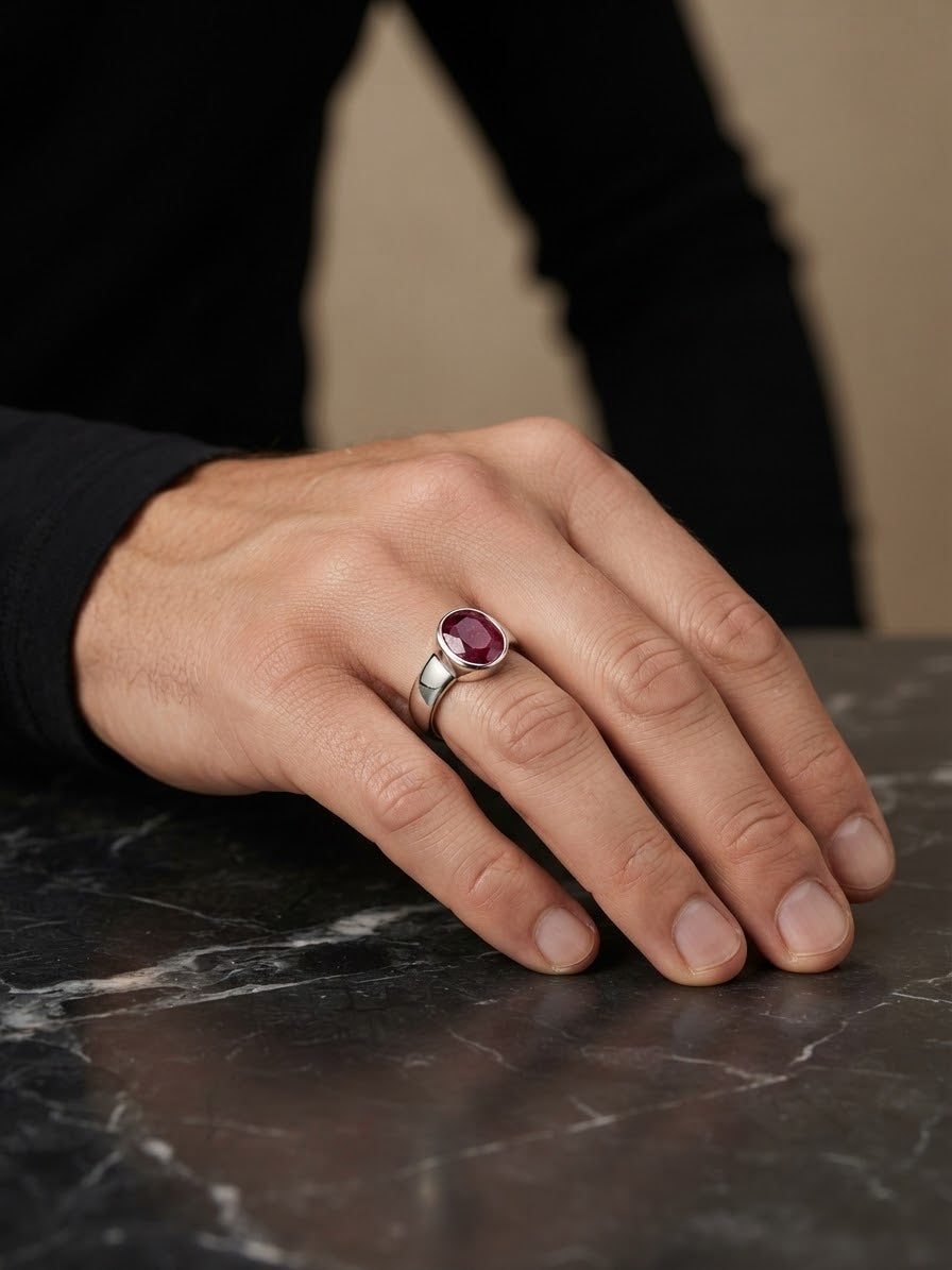 A close-up of a hand wearing a silver ring with a round purple gemstone, resting on a dark marble surface.