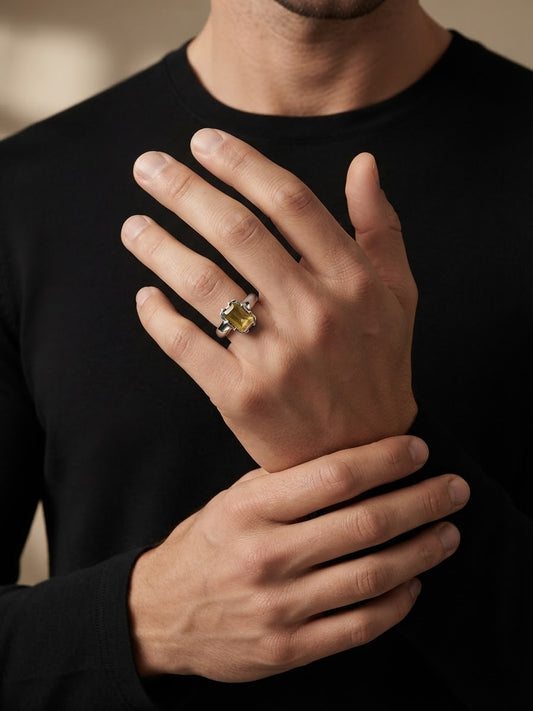 A close-up of a man's hand wearing a silver-toned ring with a yellow gemstone, set against his black shirt.
