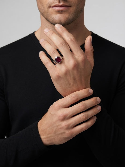 A close-up of a man wearing a black long-sleeve shirt, showcasing a silver ring with a round red gemstone on his ring finger.
