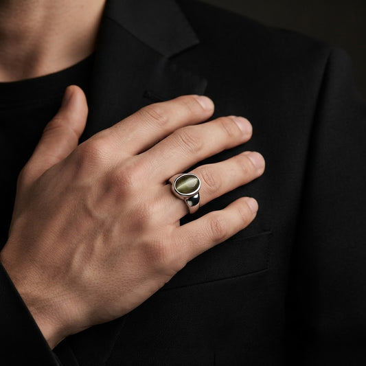 A close-up of a man's hand resting on his black suit jacket, wearing a silver signet ring with a polished oval green stone.