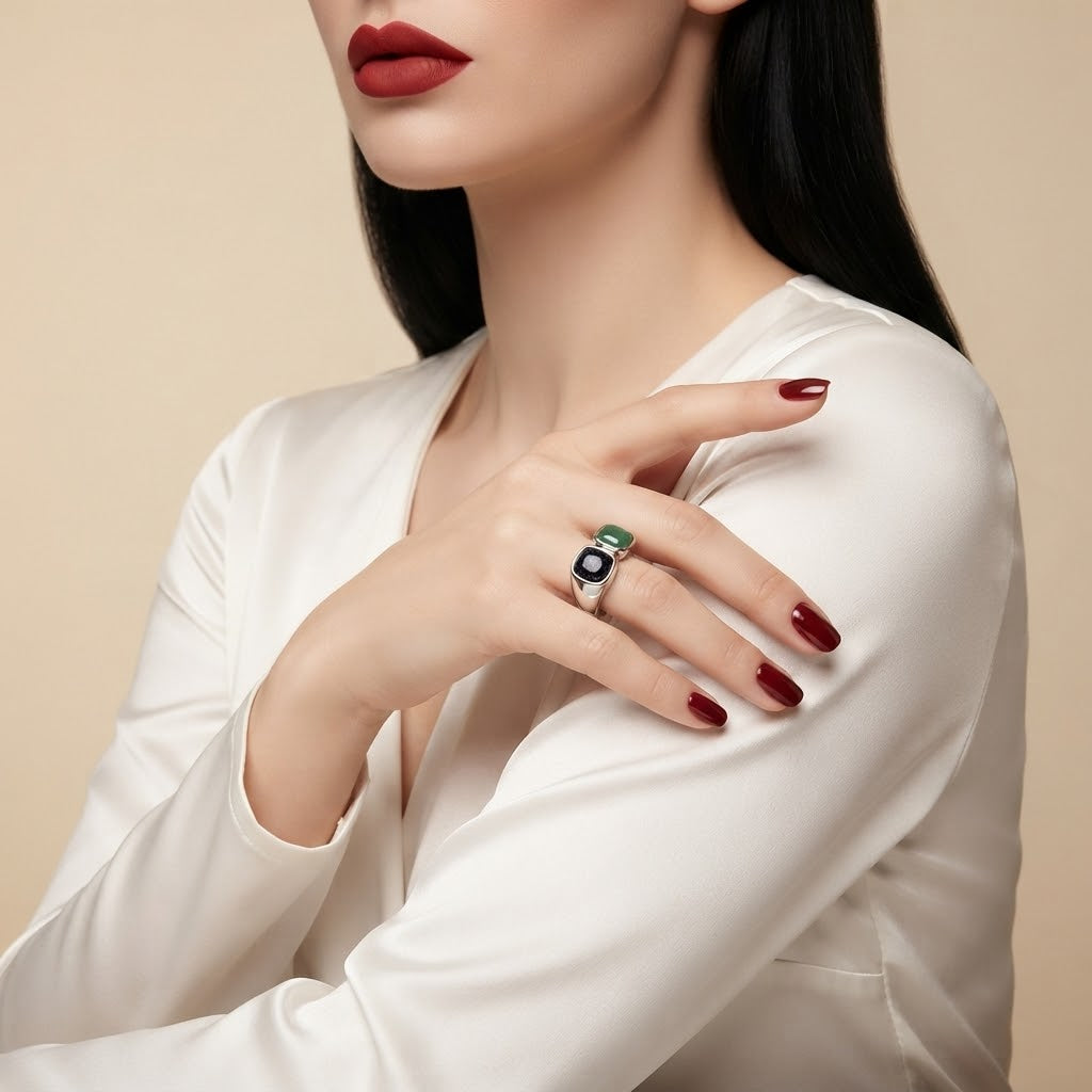 A close-up of a model wearing a silver ring with a green and black square inlay, styled with a white satin blouse against a beige background.