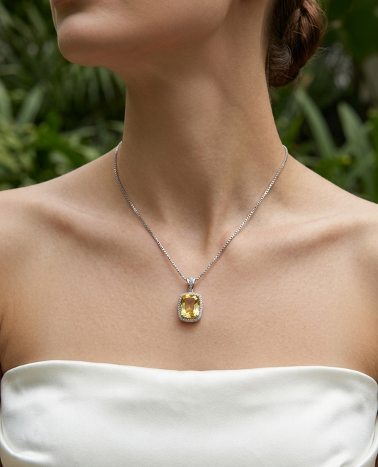 Necklace with a yellow gemstone pendant worn by a person in a white strapless top, with a blurred green background.