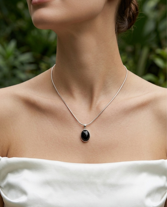 Necklace with a black pendant worn by a person against a blurred green background