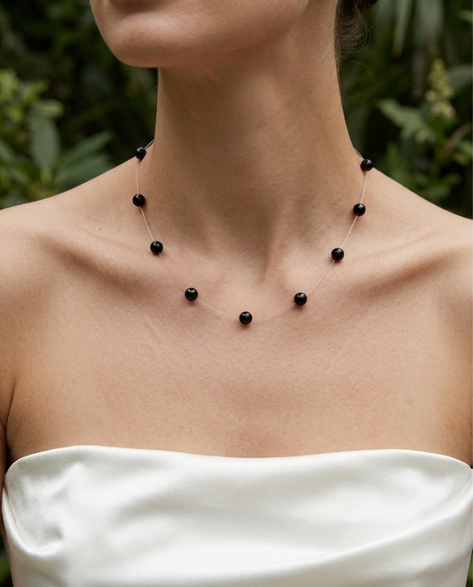 Necklace with black beads on a person wearing a white top against a blurred green background