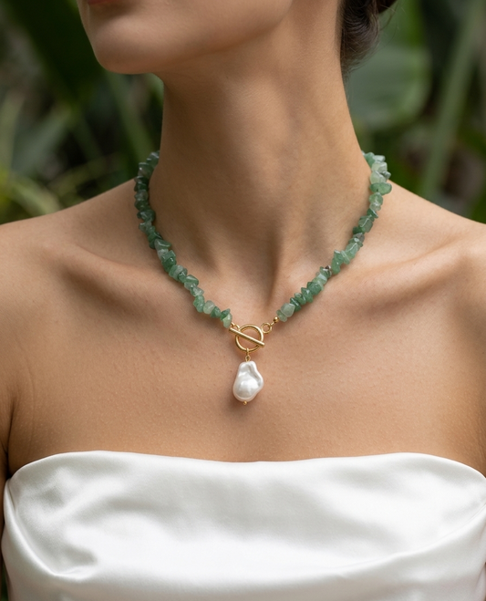 Necklace with green beads and a pearl pendant worn by a person in a white top.