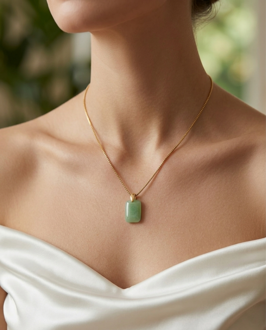 Necklace with a green pendant worn by a person in a white top, blurred greenery in the background