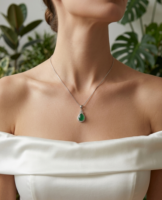 Person wearing a necklace with a green pendant against a blurred natural background