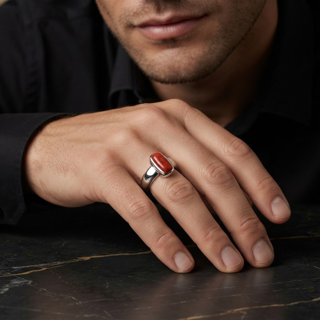 A close-up of a man's hand resting on a dark marble surface, wearing a silver ring with a polished red oval cabochon stone.