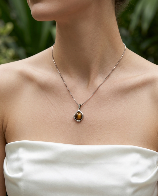 Necklace with a pendant worn by a person in a white strapless top, with a blurred natural background.