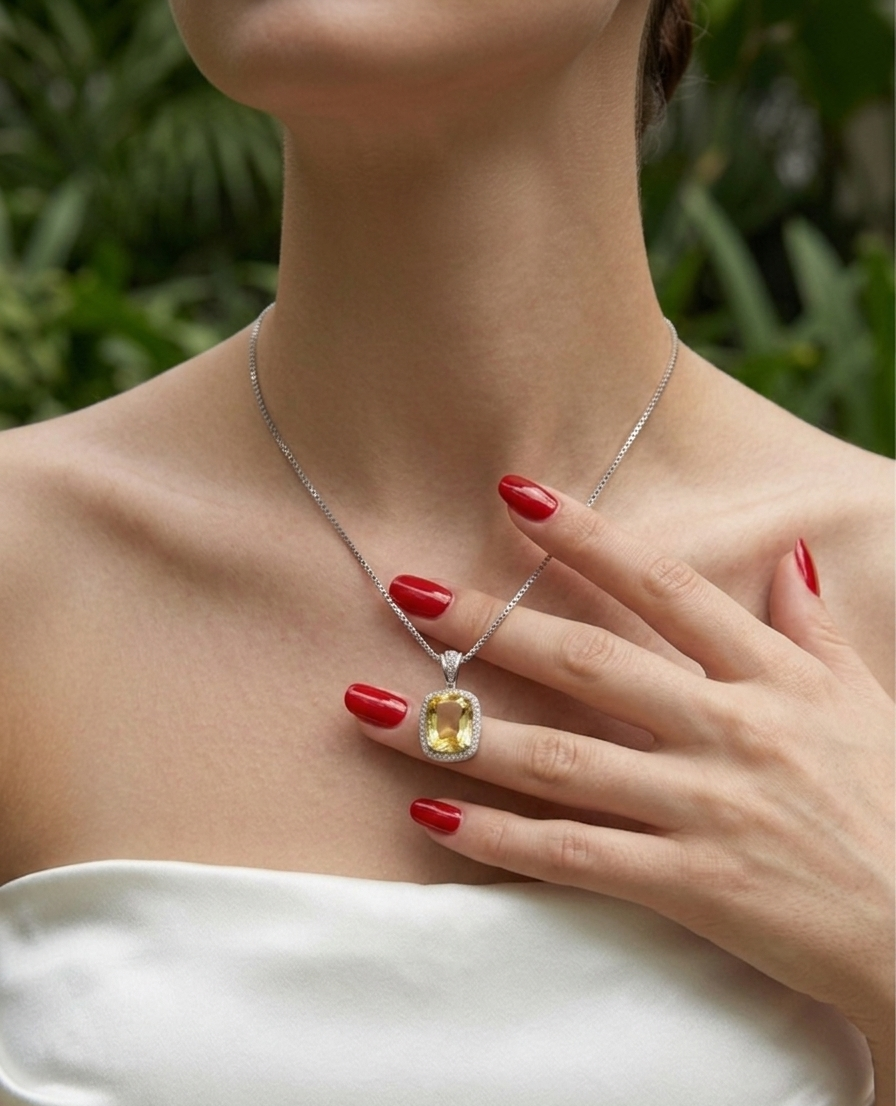 Woman wearing a silver necklace with a yellow gemstone, holding her hand to her chest.