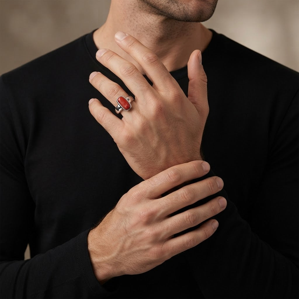 A close-up of a man wearing a black long-sleeve shirt, showcasing a silver ring with a polished red stone on his ring finger.