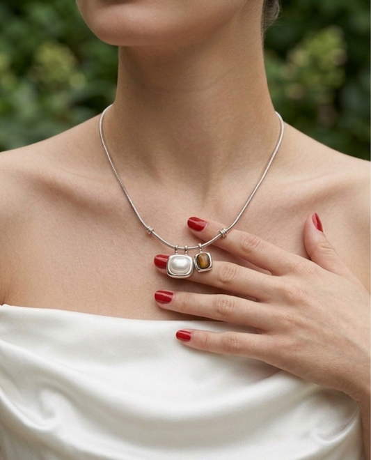 Woman wearing a silver necklace with a pendant, holding her hand to her chest.